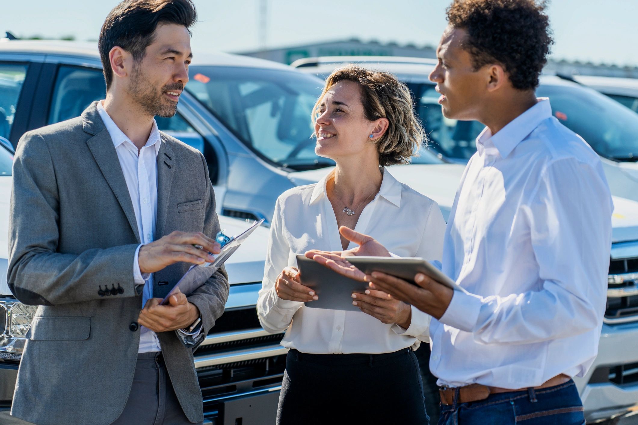 Dealership coworkers discussing inventory and details on a tablet in a parking lot