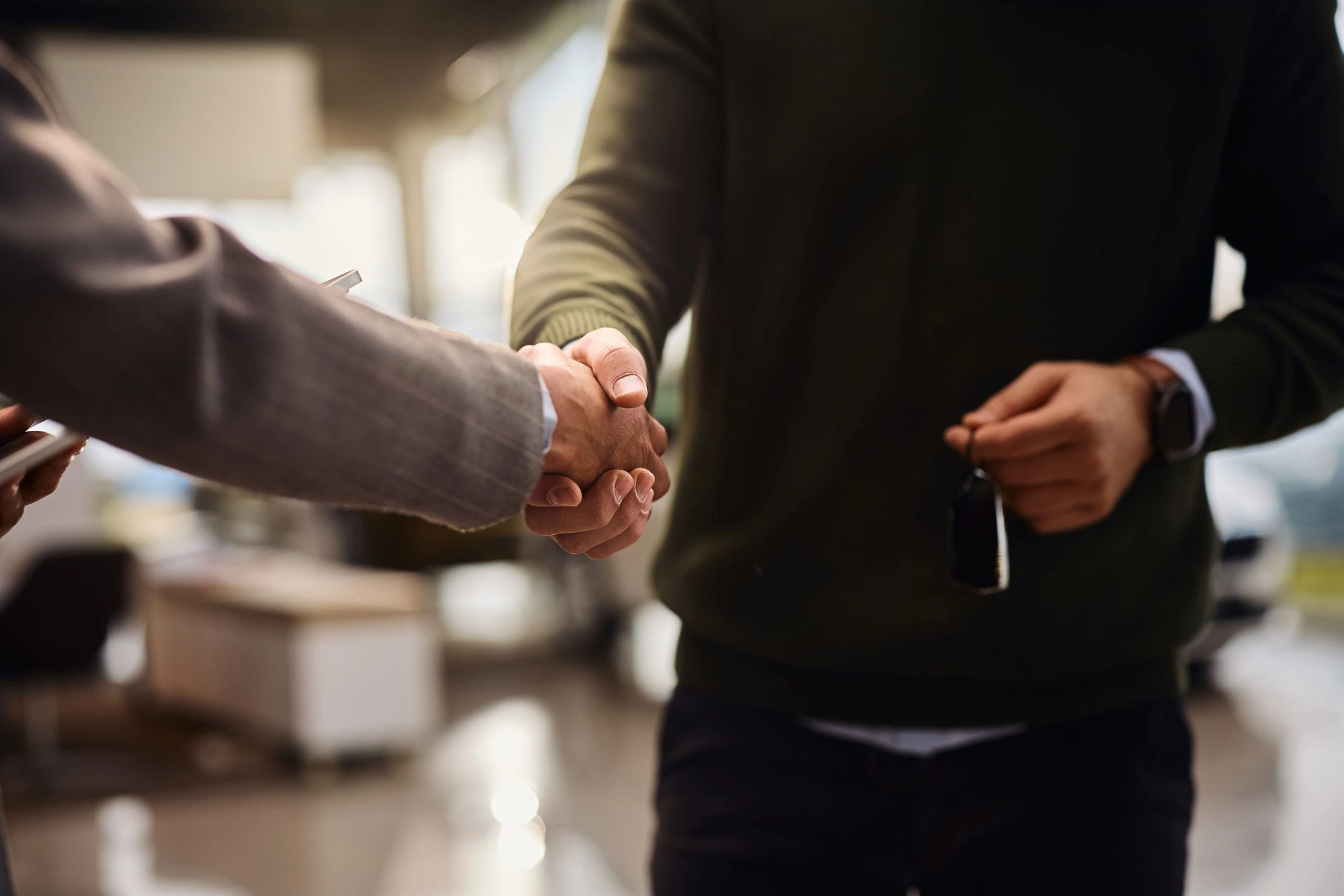 Close-up of a buyer and car salesperson shaking hands in a showroom